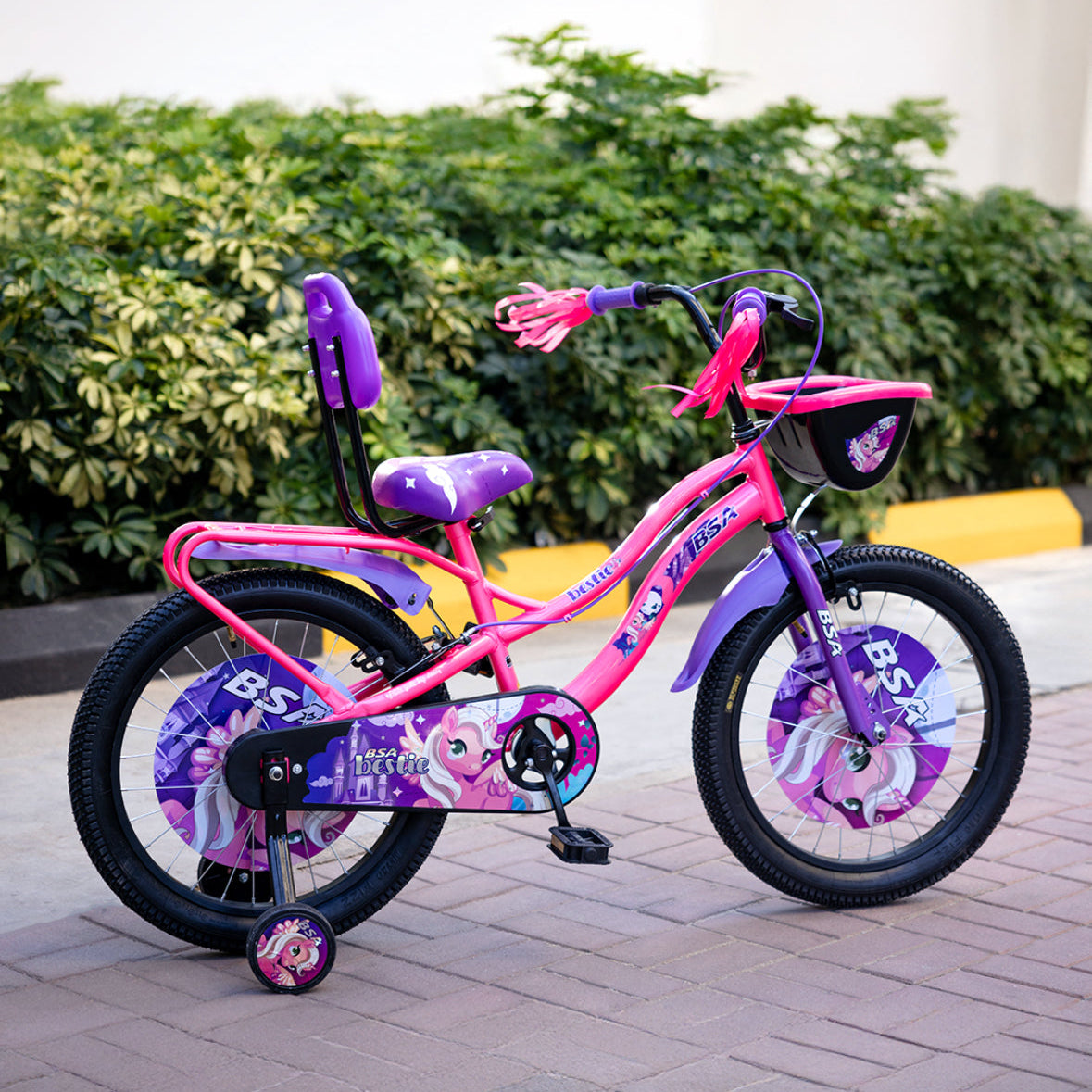 Pink children's bicycle with purple accents on a paved surface with greenery in the background