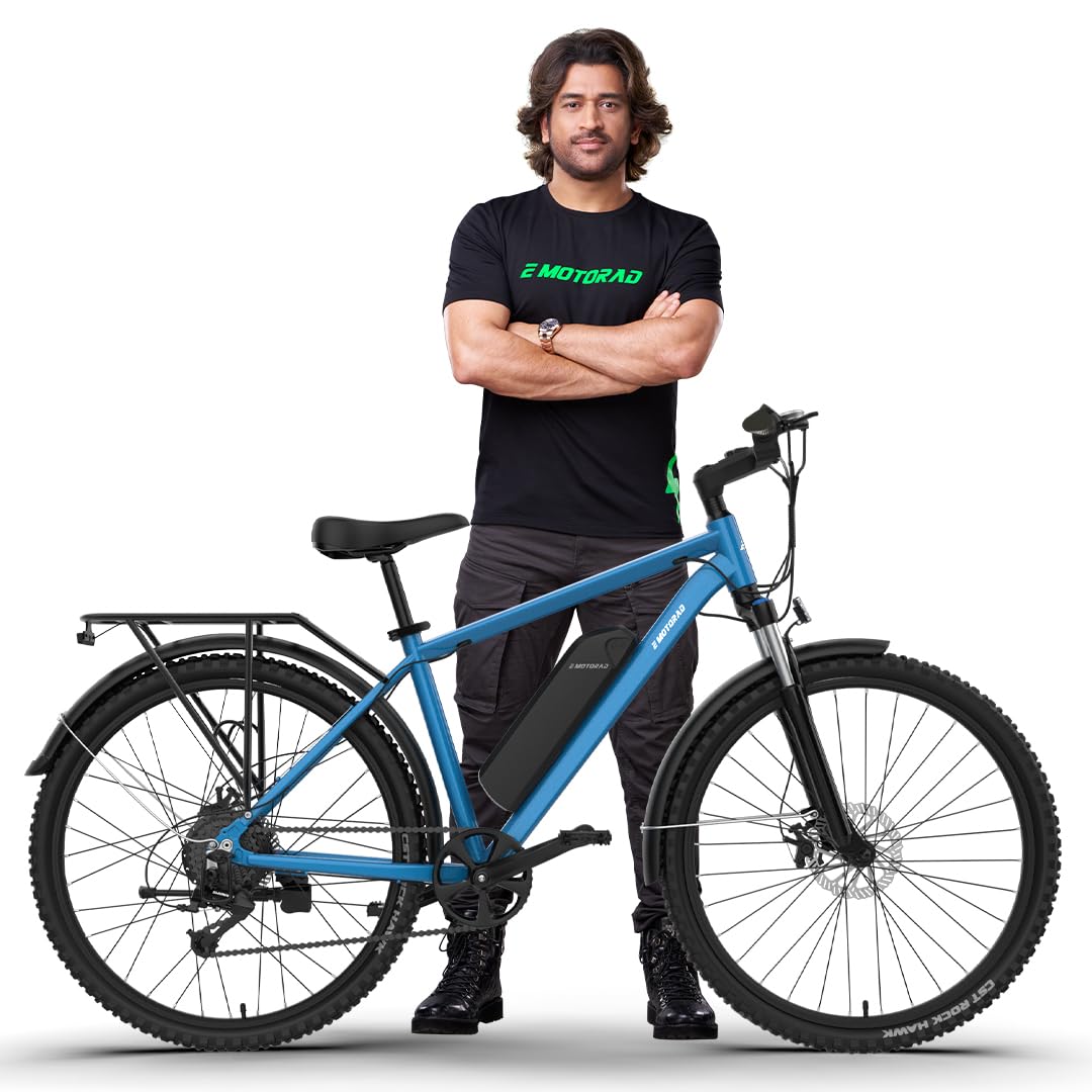 MS Dhoni standing with EMotorad T-Rex Pro Electric Cycle in Ocean Blue color featuring front suspension, rear rack, and battery integrated frame
